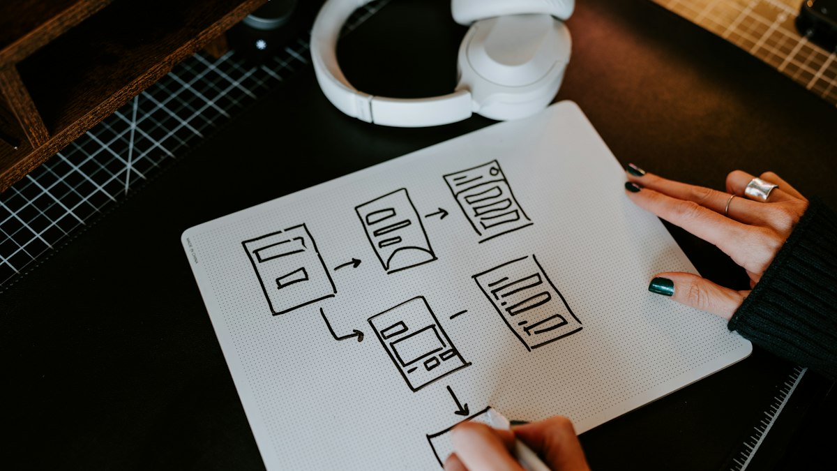 Hand sketching a website user flow on a dark desk